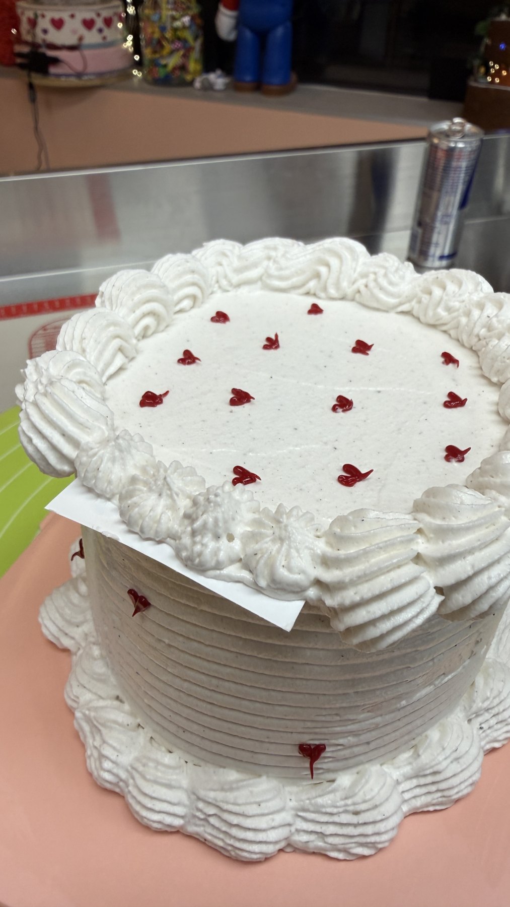 Gâteau rond décoré de crème blanche avec petits coeurs rouges.