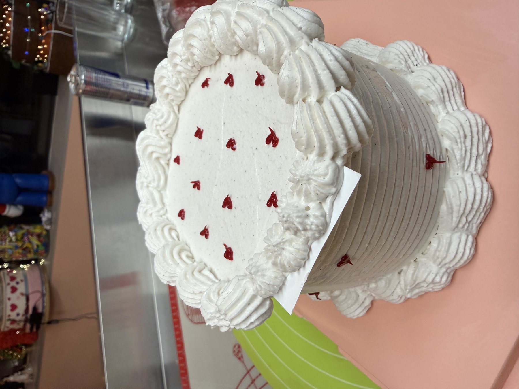 Gâteau rond décoré de crème blanche avec petites touches rouges et bordures en pochage.